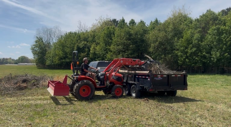 Red wood chipper machine towed behind tractor in open field with forest treeline in background